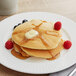 A stack of Pillsbury Old West Buttermilk pancakes with syrup and berries on a white plate.