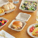 EcoChoice Natural Bagasse dinnerware on a table with a sandwich, salad, and burger.