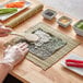 A person using the Emperor's Select Sushi Making Kit to cut sushi on a table.