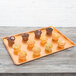 A Chicago Metallic bakery display tray with brown muffins on a wooden table.