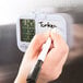 A hand writing with a white marker on a Taylor digital kitchen timer.