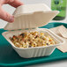 A hand holding a EcoChoice natural bagasse take-out container filled with pasta and vegetables.