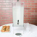A silver Cal-Mil beverage dispenser with an ice chamber and cookies on a table.