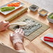 A person using an Emperor's Select sushi making kit to prepare sushi on a table.