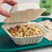 A hand holding an EcoChoice natural bagasse take-out container of food.