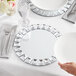 A person holding a white Acopa jeweled glass mirror charger plate with a silver fork.