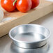 An American Metalcraft heavy weight aluminum pizza pan on a counter with tomatoes and garlic.