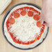 A person putting pepperoni on a pizza using an American Metalcraft hard coat anodized aluminum pizza pan.
