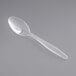 A Visions clear plastic teaspoon on a gray background.