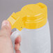A hand holding a yellow plastic Tablecraft dispenser jar with a yellow lid.