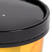 A black and yellow Huhtamaki paper soup container with a lid.