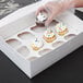 A person putting a Baker's Mark reversible cupcake insert with a cupcake in a box.