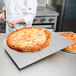 A chef using an American Metalcraft aluminum pizza peel to remove a pizza from the oven.