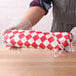 A person in gloves holding a roll of red and white checkered deli sandwich wrap paper.