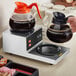 An Avantco double burner coffee decanter warmer on a counter with coffee being poured into a coffee pot.