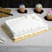 A white cake with frosting on a Enjay gold cake board on a table.