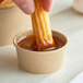 A hand dipping a churro into a cup of sauce.