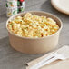 A round kraft paper take-out bowl filled with macaroni and cheese.