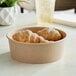 A Choice kraft paper take-out bowl filled with croissants on a table.