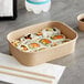 A rectangular kraft paper take-out container filled with sushi on a table.