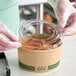A plastic gloved hand placing an EcoChoice compostable PLA lid on a container of food.