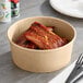 A Choice kraft take-out container filled with food on a table with a bowl of ribs and a fork.