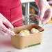 A gloved hand holding an EcoChoice rectangular compostable plastic lid on a container of food.