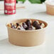A kraft paper take-out container filled with chocolate covered doughnuts on a table.