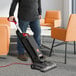 A person using a Hoover Task Vac 2 commercial bagged upright vacuum cleaner to clean carpet in an office.