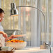 A woman using a stainless steel Avantco heat lamp to serve herself pasta from a hotel buffet.