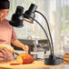 A woman in a chef's hat using an Avantco dual arm heat lamp to cut a piece of bread.