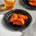 A Huhtamaki Chinet black plastic plate with chicken wings and a glass of beer.