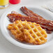 A plate of Lamb Weston Waffled Hash Brown Potatoes with bacon and waffles.