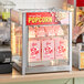 A ServIt countertop display warmer filled with boxes of popcorn with red text.
