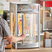 A person standing next to a ServIt countertop display warmer filled with churros.