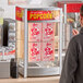 A man standing in front of a ServIt countertop display warmer filled with popcorn boxes.
