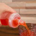A hand pouring orange liquid from a GET bottle into a glass.