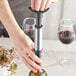 A hand using an Acopa stainless steel vacuum wine pump to preserve a bottle of red wine.