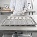A person in a white uniform using a Chicago Metallic Rounded End Hoagie Bun Pan to bake bread dough.