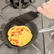 A hand using a spatula to cook an omelette in a Vollrath Optio stainless steel non-stick fry pan.