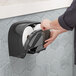 A person using a Tork black double roll toilet paper dispenser.