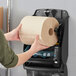 A person holding a roll of Tork Universal natural kraft paper towels.