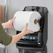 A hand holding a Tork Universal white paper towel roll.