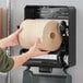 A person holding a Tork Universal notched paper towel roll in front of a roll holder.