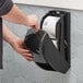 A man using a Tork black double roll toilet paper dispenser.
