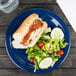 A Carlisle Dallas Ware blue melamine plate with a hot dog and salad on it.