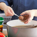 A person stirring brown Knorr Professional Select Beef Base into a bowl of food.