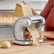 A woman using an Imperia Pasta Presto machine to make pasta with a ball of dough on a table.