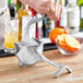 A person using a Barfly aluminum juicer to juice an orange over a glass.