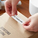 A person putting a Lavex white thermal transfer label on a cardboard box.
